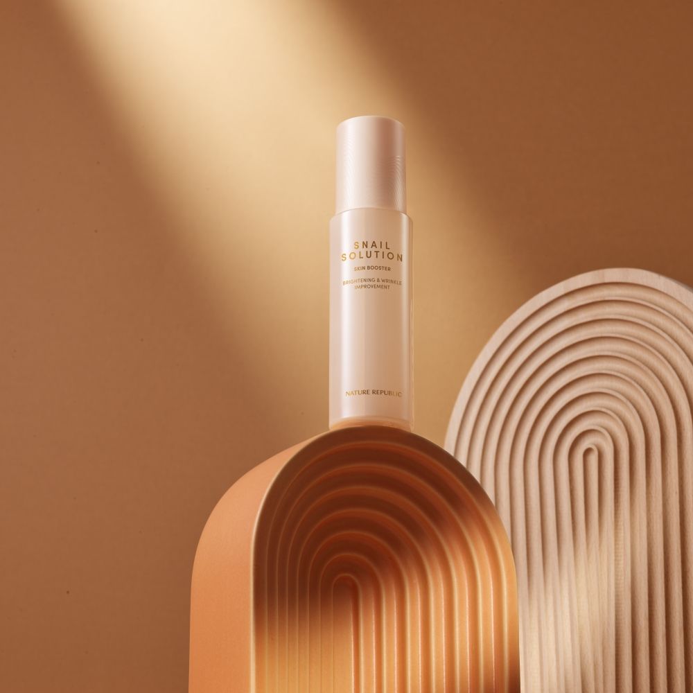 Beige Flasche Snail Solution Skin Booster auf Podest. Aufschrift: NATURE REPUBLIC. Hintergrund: beige und braun.