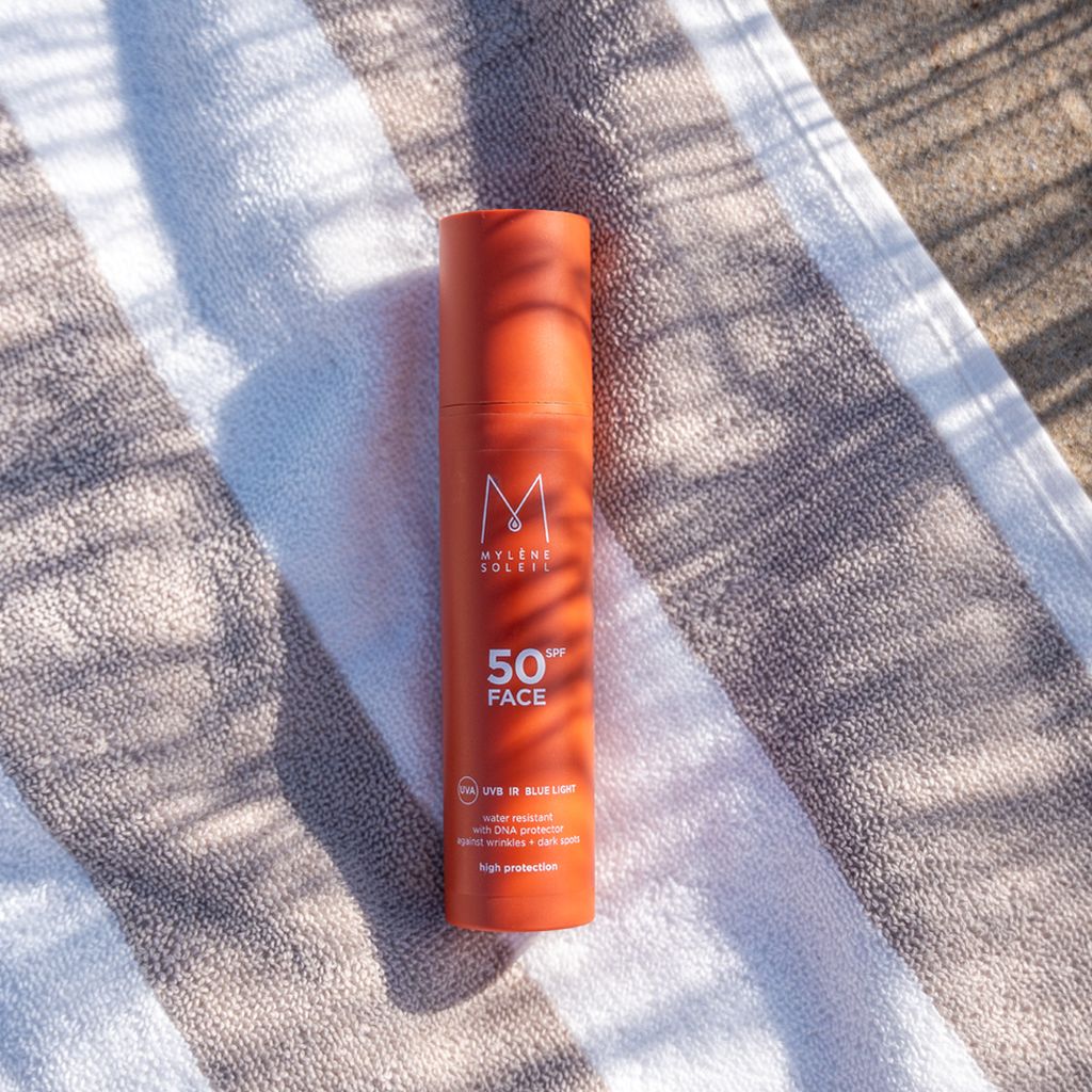 Mylène Soleil SPF 50 Face Sonnenlotion auf einem gestreiften Handtuch im Freien.