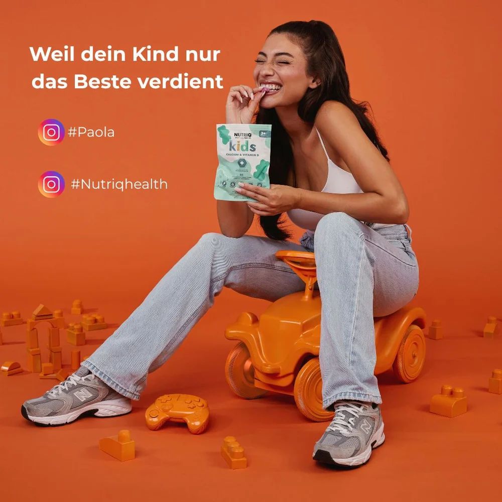 Frau sitzt auf einem Spielzeugauto. Hält eine Packung NUTRIQ kids Calcium & Vitamin D3. Instagram-Namen: #Paola, #Nutriqhealth.