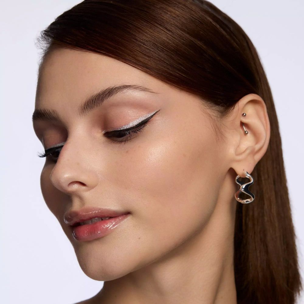 Nahaufnahme eines Gesichts mit silbernem Eyeliner. Geschlossene Augen, rosige Lippen.