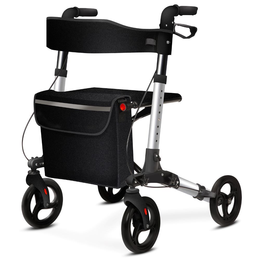 Rollator mit schwarzem Sitz, Einkaufstasche und Rückengurt. Vier Räder, silberfarbenes Gestell. Stockhalterung nicht sichtbar.
