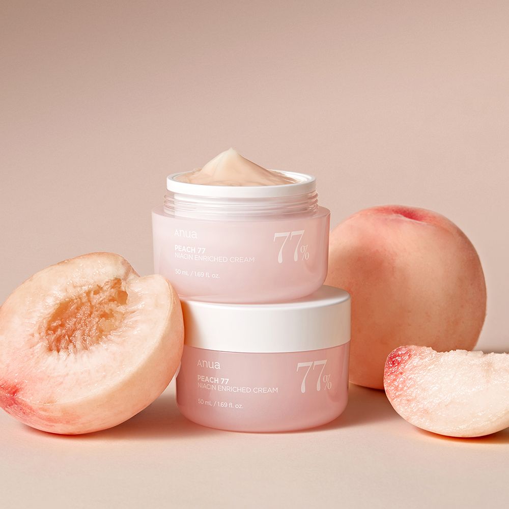 Zwei ANUA Peach 77% Niacin Enriched Cream Tiegel, umgeben von frischen Pfirsichen.