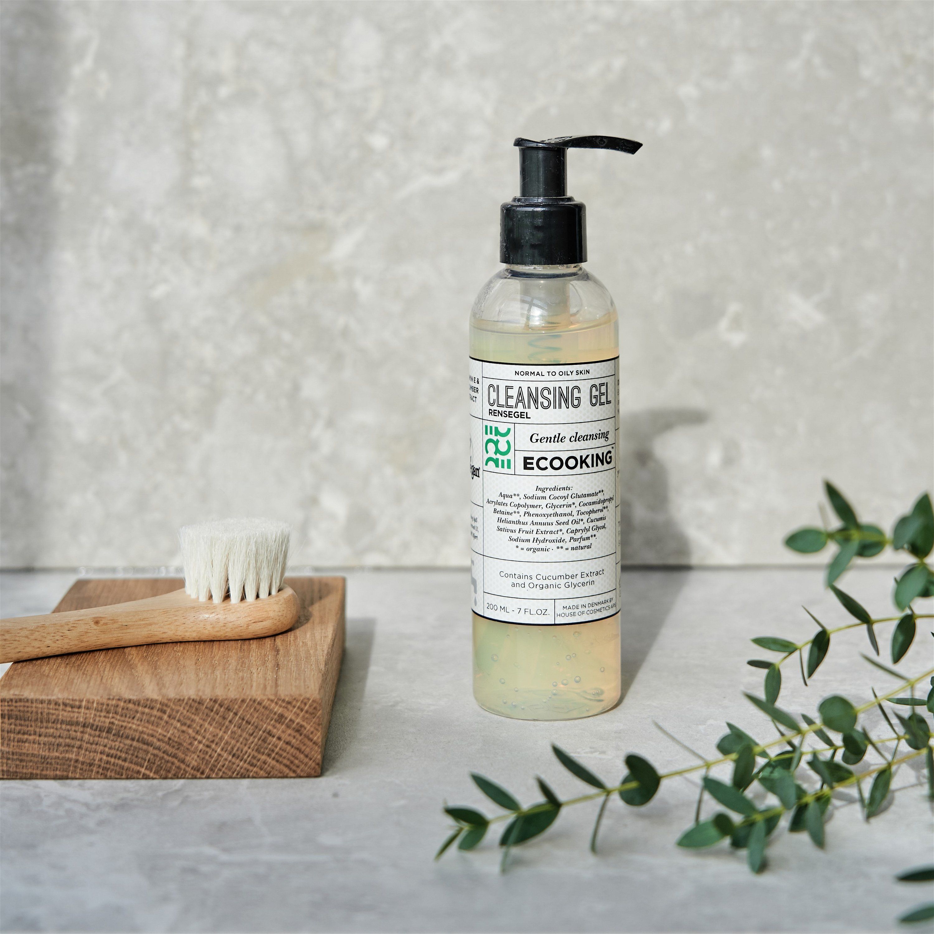Reinigungsgel-Flasche mit schwarzem Pumpverschluss. Aufschrift: Cleansing Gel, Ecooking. Neben Holzbrett mit Bürste und Zweig mit Blättern.