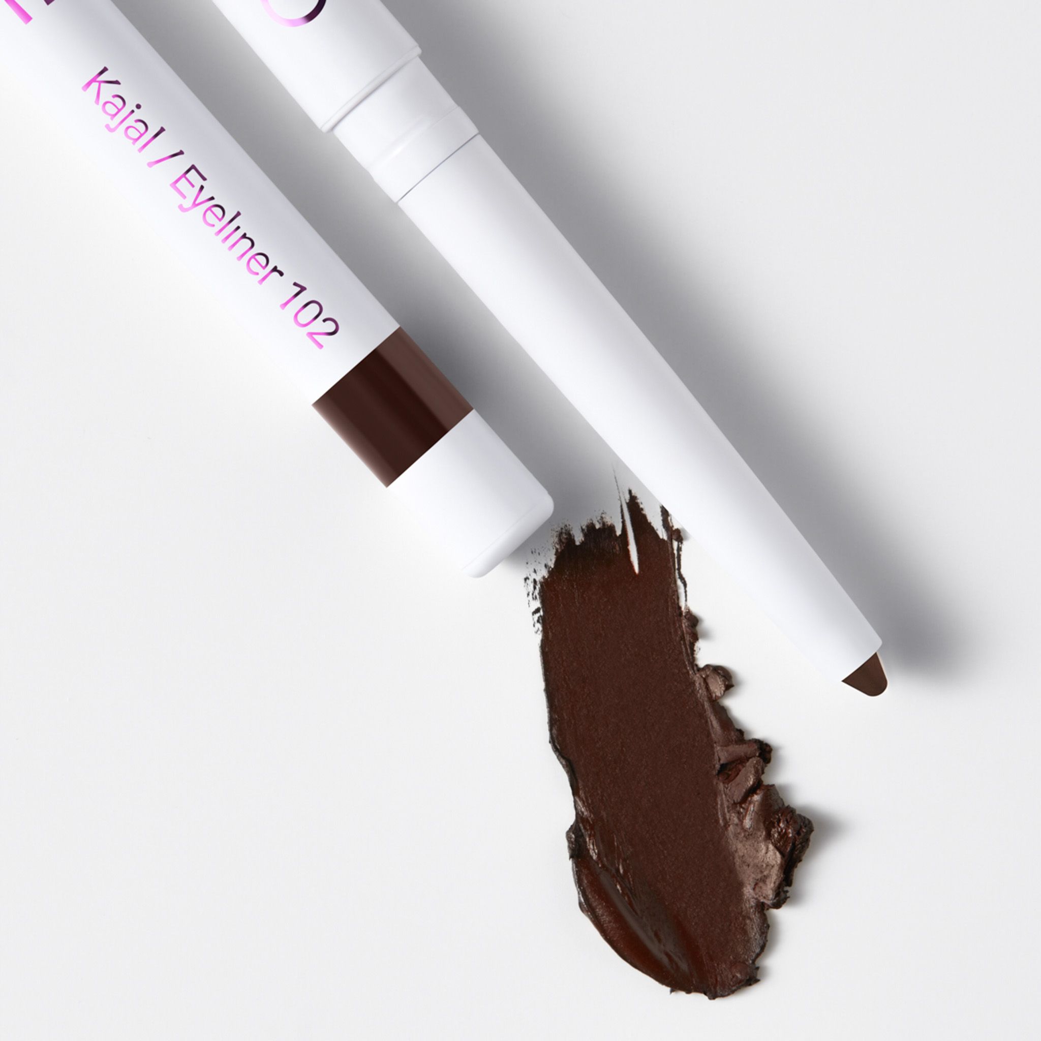 Zwei weiße Kajal-Eyeliner-Stifte mit brauner Mine und ein brauner Farbfleck. Aufschrift: "Kajal / Eyeliner 102".