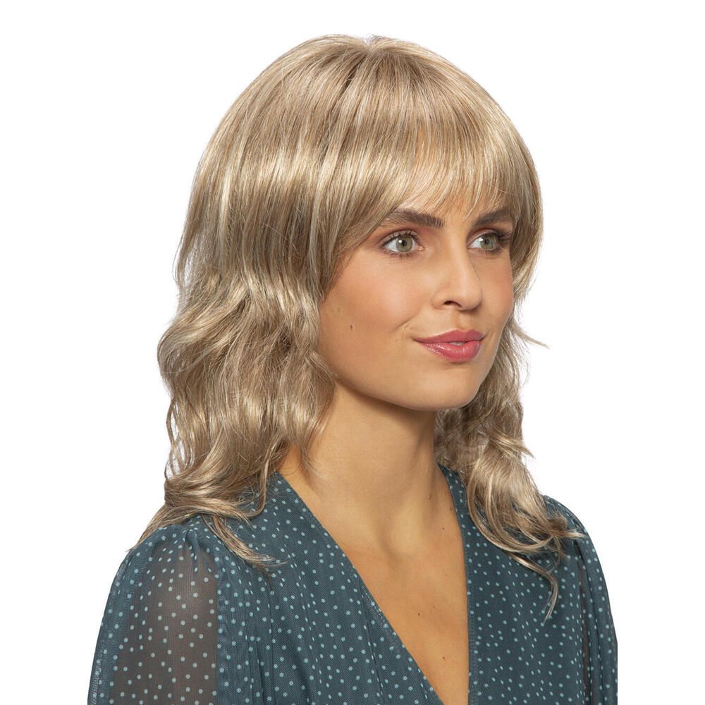 Perücke mit Pony und gewelltem Haar. Blond mit helleren Strähnen. Frau mit grünem Oberteil.