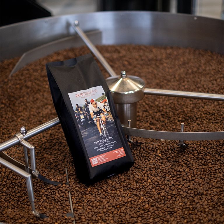 Kaffeepackung BERGBRAND Eddy Would Attack in einem Röster. Kaffeebohnen umgeben die Packung.