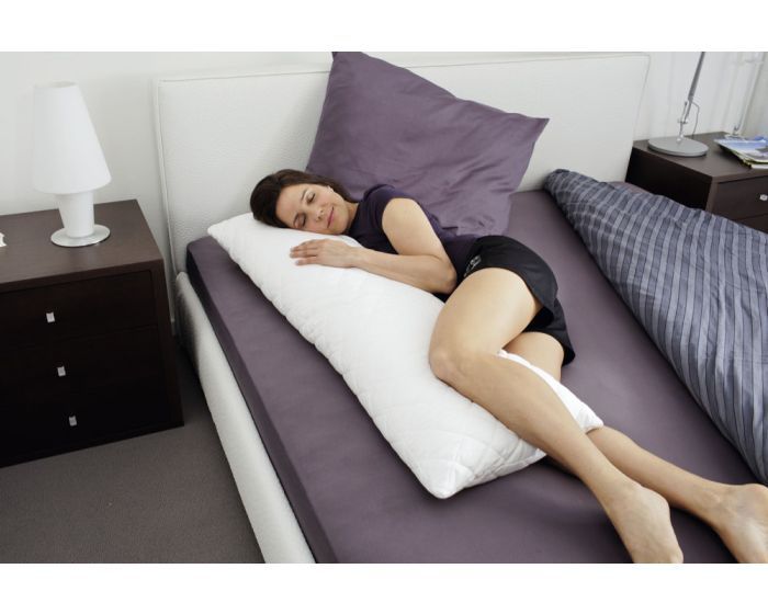 Person liegt auf einem Bett mit einem weißen Seitenschläferkissen. Kissen ist unter dem Körper platziert.