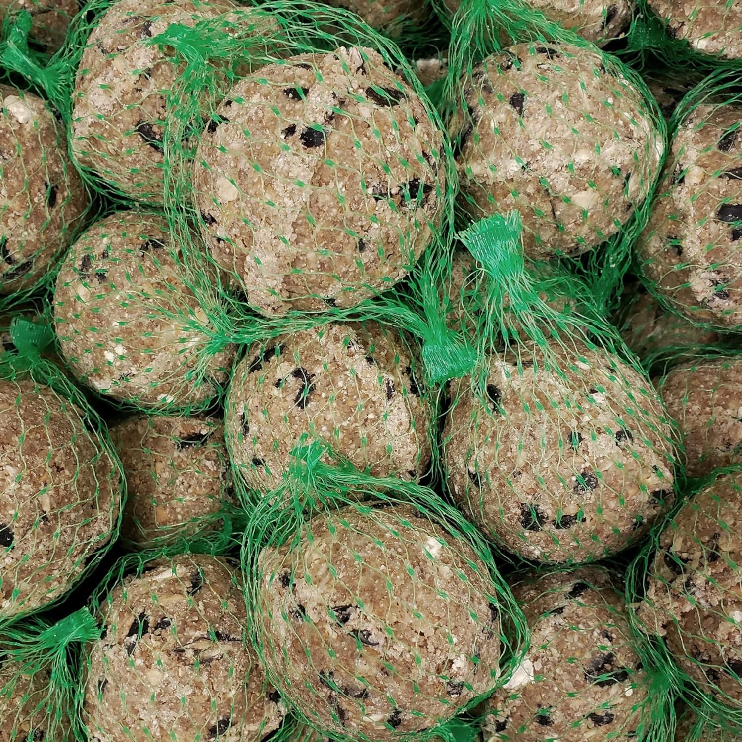 Nahaufnahme von mehreren Meisenknödeln in grünen Netzen. Braune und schwarze Bestandteile sichtbar.