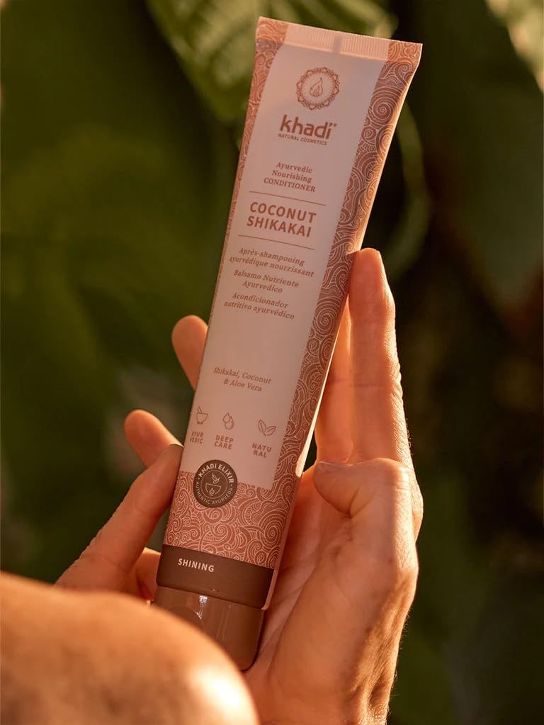 Person hält Khadi Kokos Shikakai Conditioner Tube. Beige-braunes Design mit Produktnamen und Inhaltsstoffen. Ayurveda-Zertifizierung.