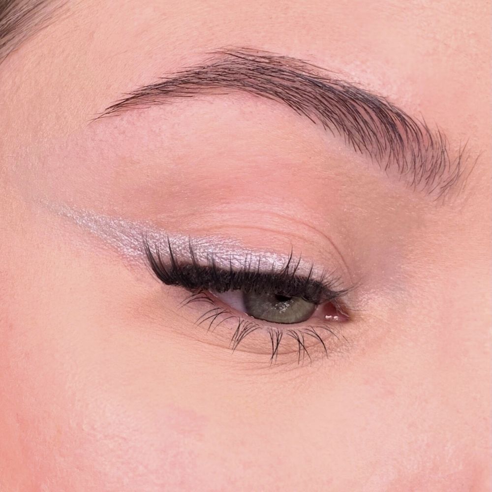 Auge mit silberfarbenem Eyeliner. Wimpern und Augenbrauen sichtbar. Hautton rosa.