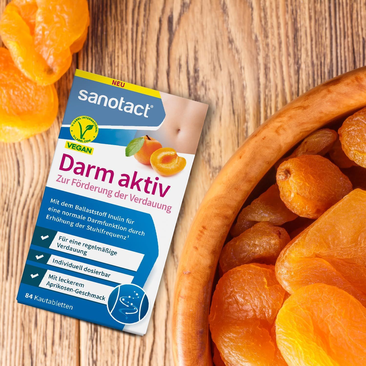 Sanotact Darm aktiv Kautabletten. Verpackung neben getrockneten Aprikosen. Vegan-Logo. 84 Kautabletten.