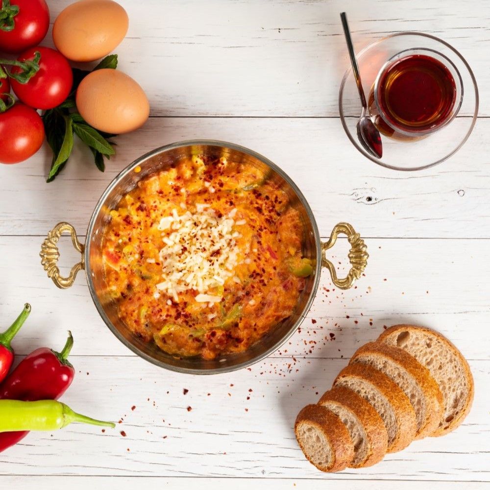 Gericht in Metallpfanne mit goldenen Griffen. Enthält Eier, Tomaten, Paprika. Brot, Tee.