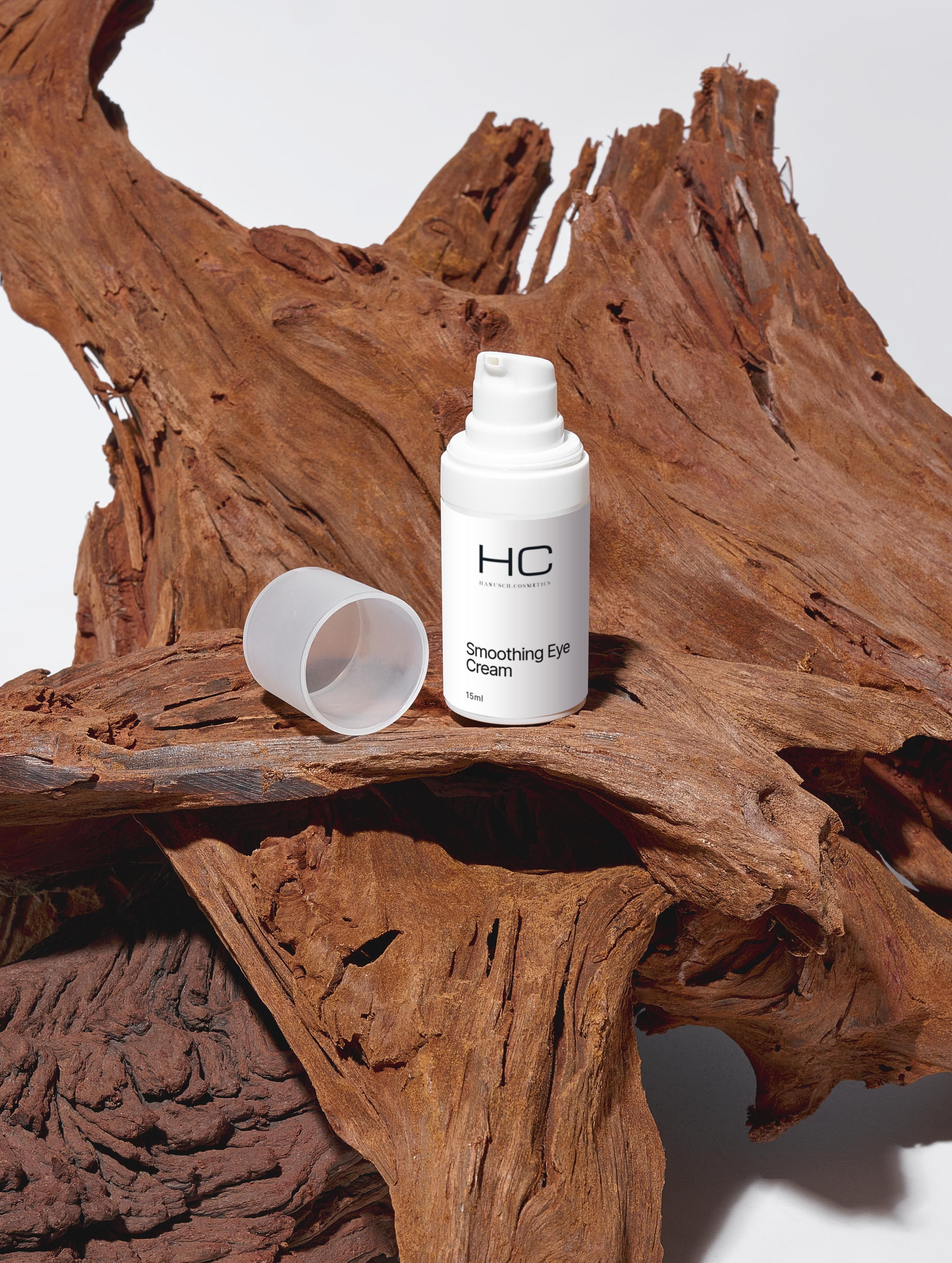 Weiße Flasche mit "HC Hanusch Cosmetics Smoothing Eye Cream" auf Holz. Offener Deckel.