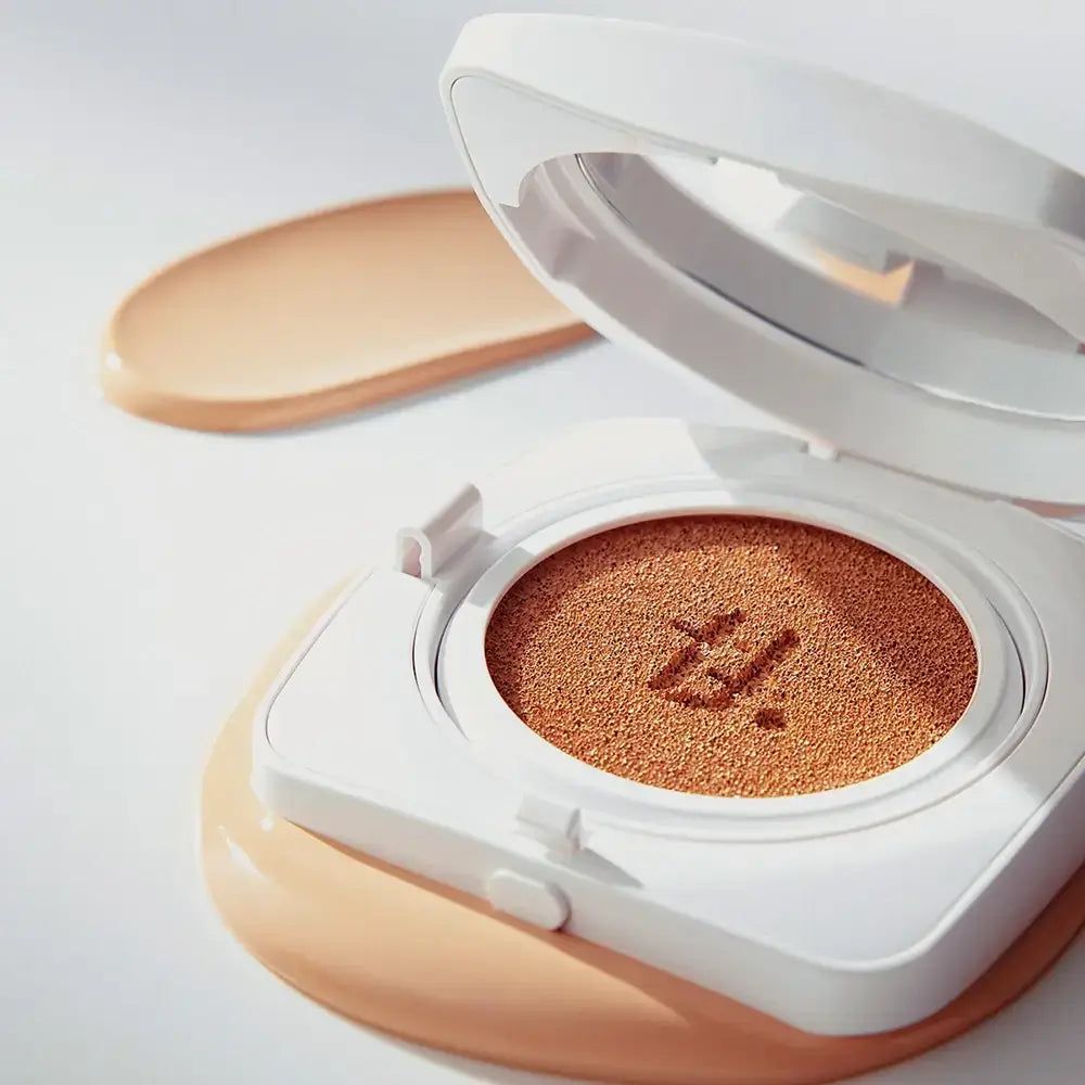 Weißer Cushion-Kompakt-Make-up-Behälter mit Spiegel. Geöffnet, mit Schwamm und Make-up. Daneben ein Make-up-Abstrich.