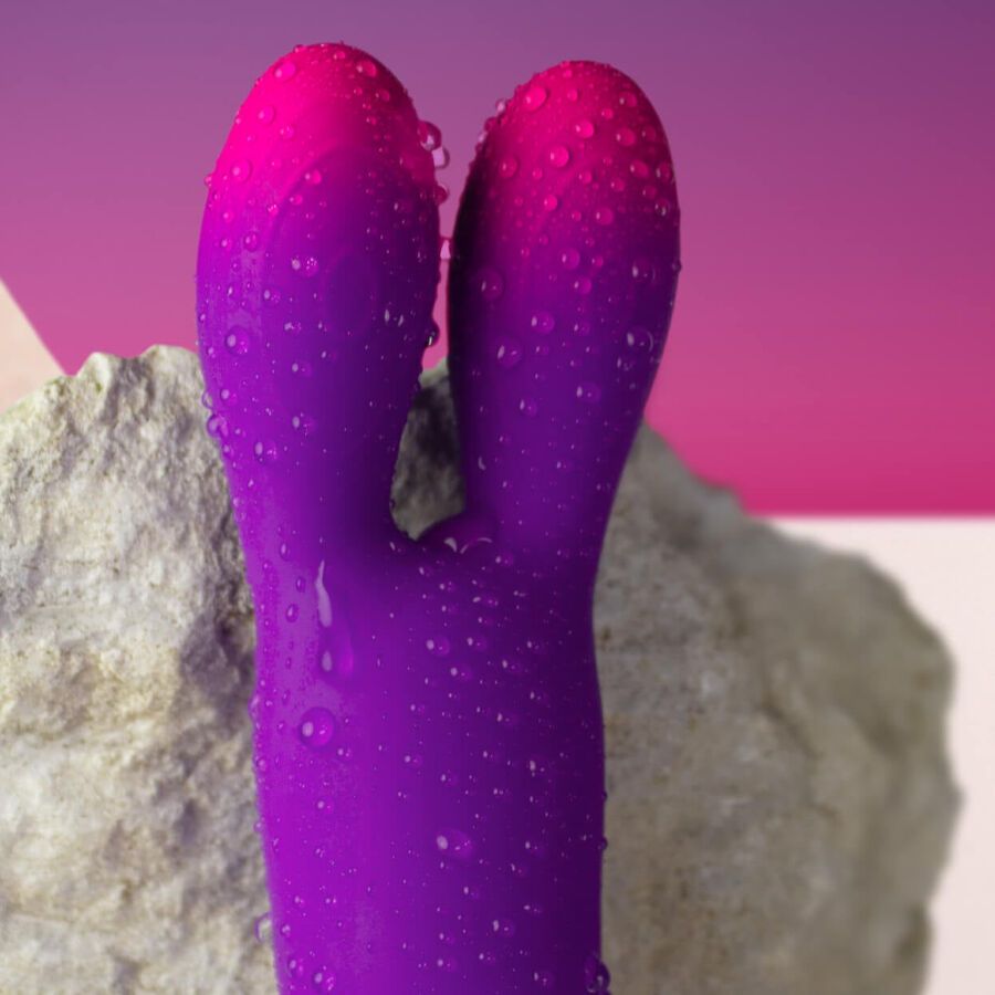 Lila Vibrator mit Hasenohren-Design. Farbverlauf von Lila zu Pink. Mit Wassertropfen. Auf Stein platziert.