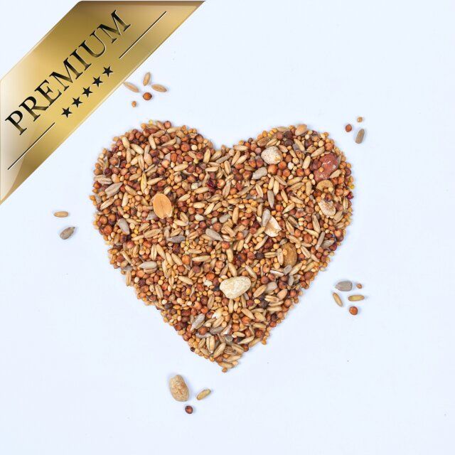Streufutter in Herzform auf weißem Grund. Goldenes Band: PREMIUM. Einige Körner verstreut.