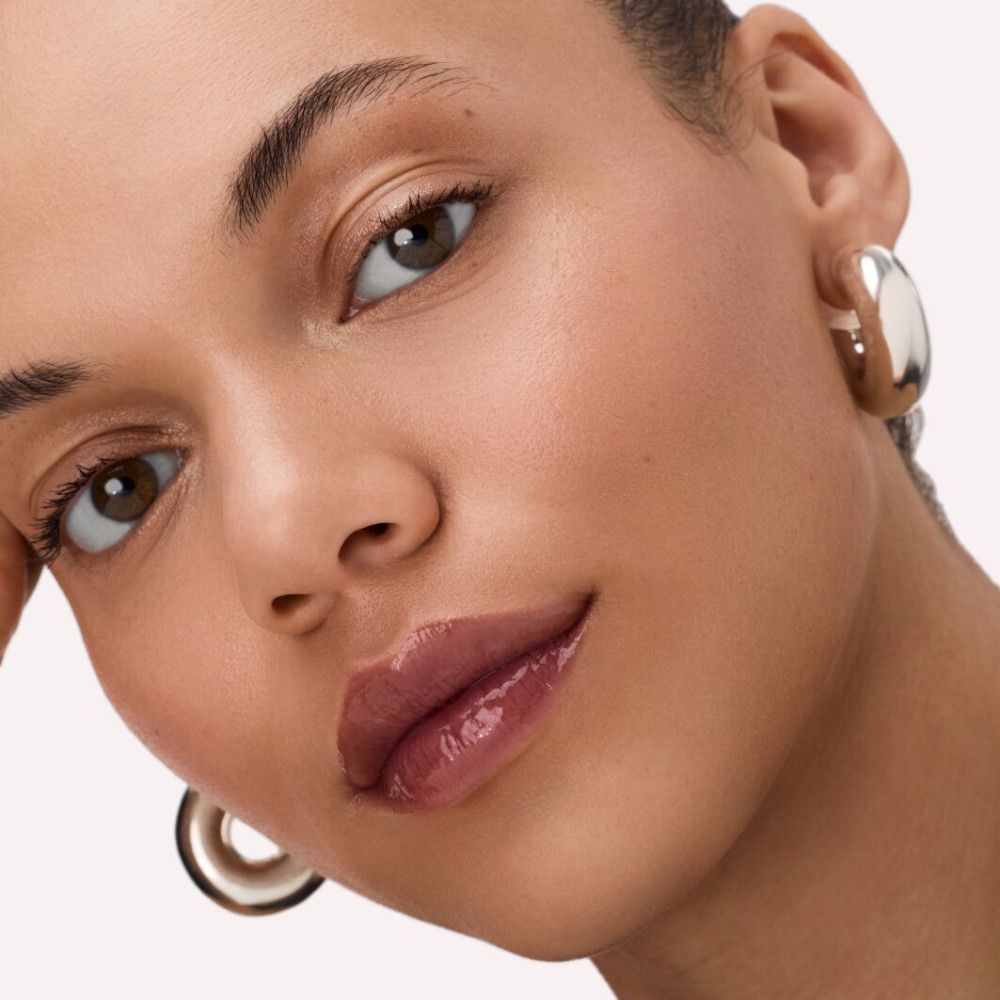 Porträt einer Person mit glänzendem Lippenbalsam. Hautton: hellbraun. Silberne Ohrringe.