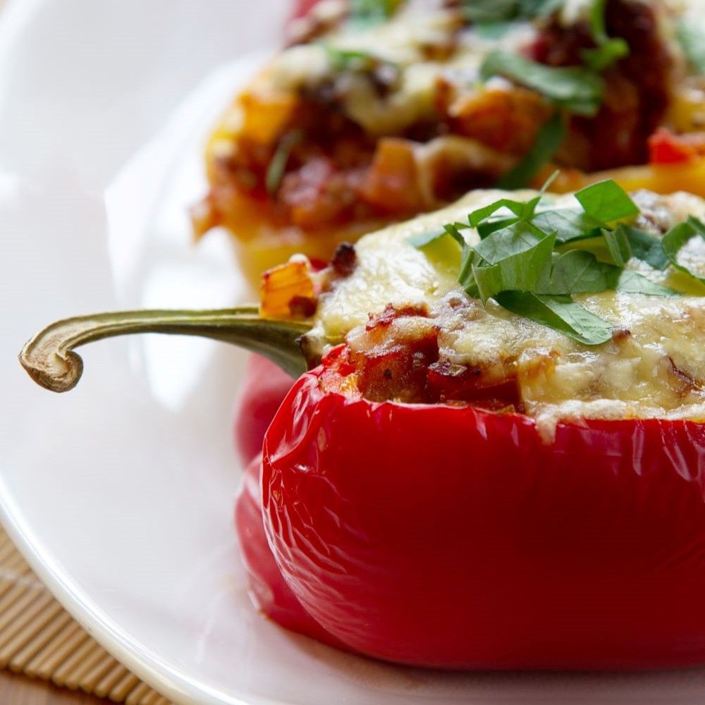 Gefüllte rote Paprika auf weißem Teller. Käse und Kräuter auf der Füllung.