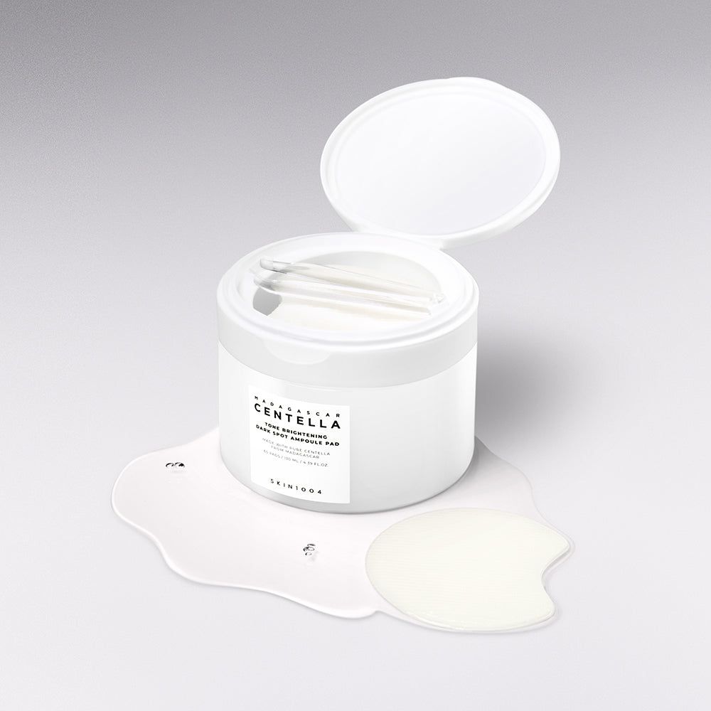 Offener Behälter mit SKIN1004 Madagascar Centella Ampoule Pads, Pinzette und verschüttetem Serum daneben.