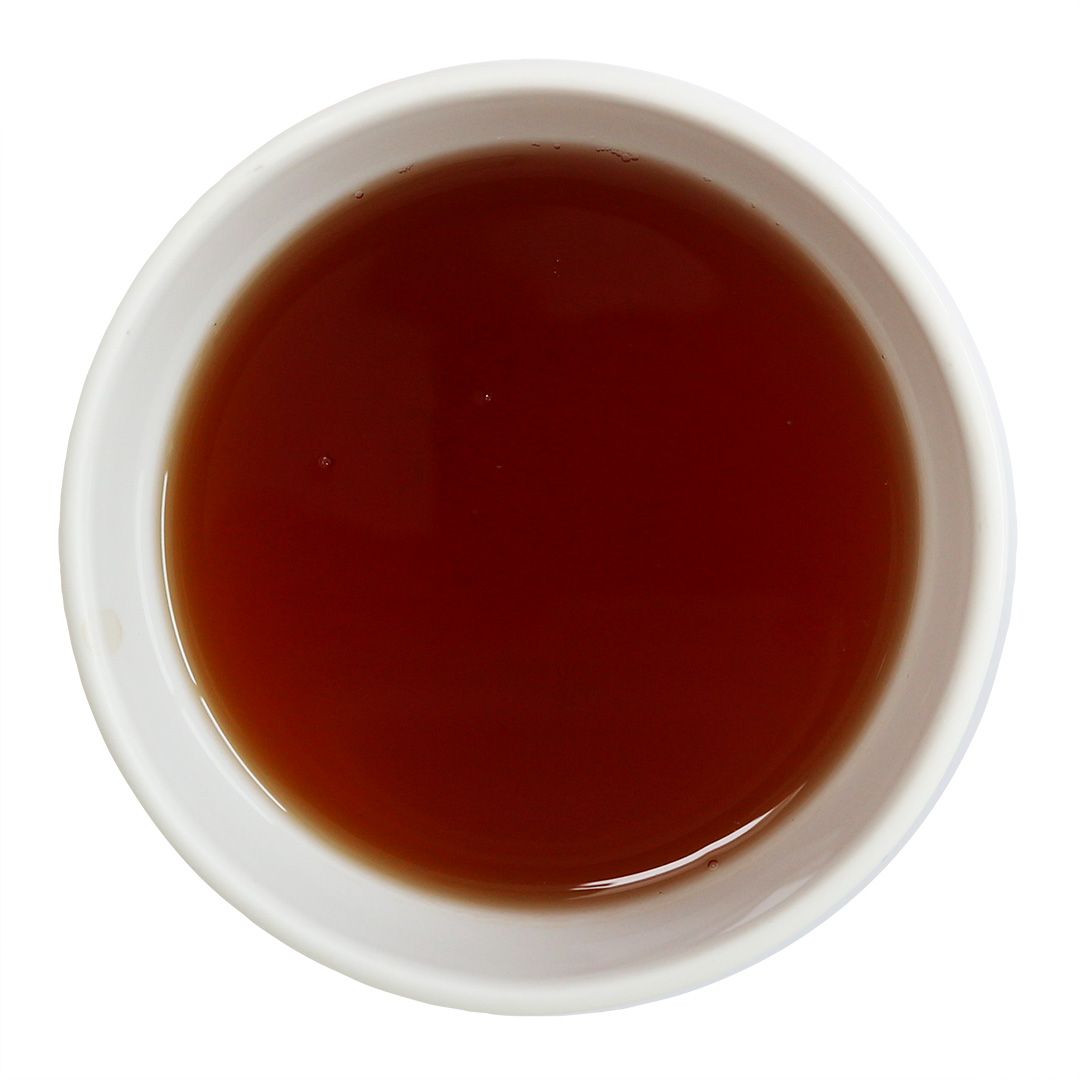 Eine weiße Schale mit braunem Tee. Der Tee ist flüssig und spiegelt sich in der Schale wider. Der Hintergrund ist weiß.