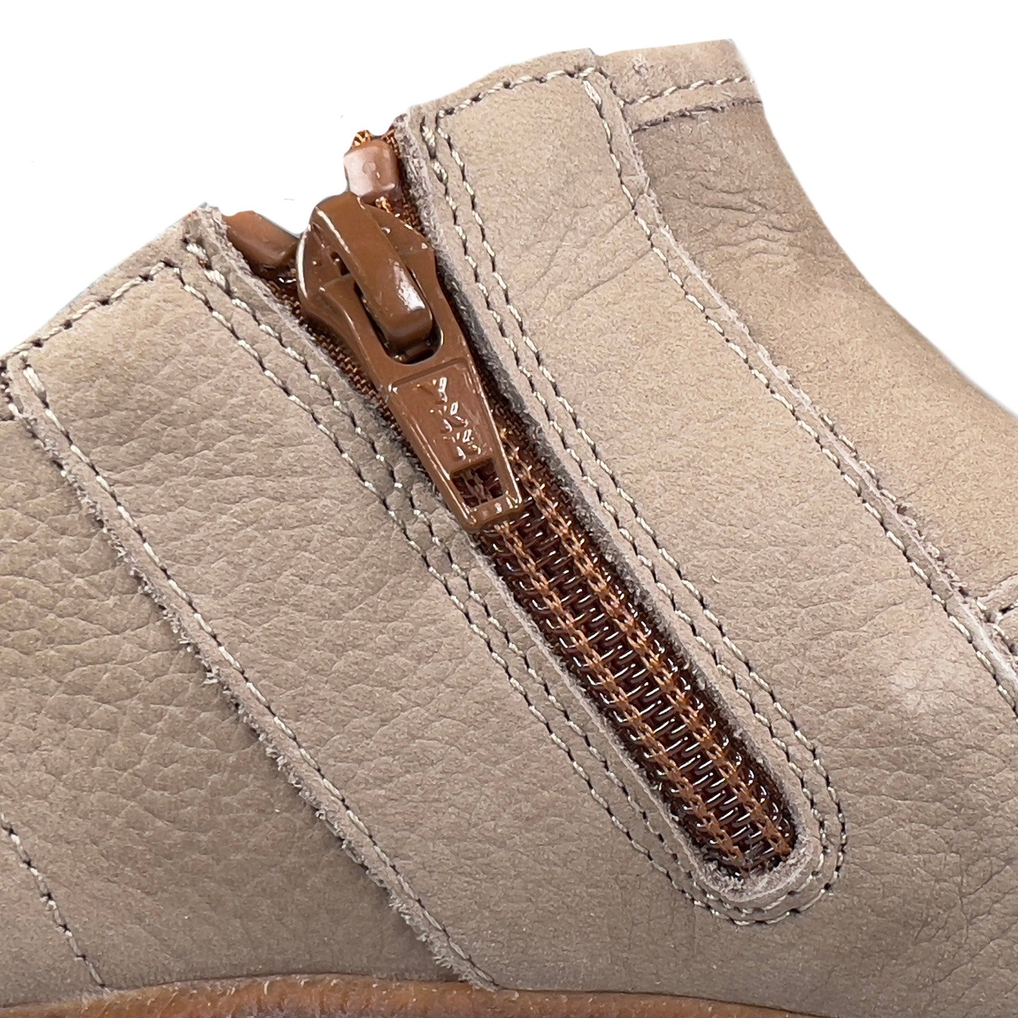 Nahaufnahme eines Schuhs mit braunem Reißverschluss. Beige Lederstruktur, sichtbare Nähte.