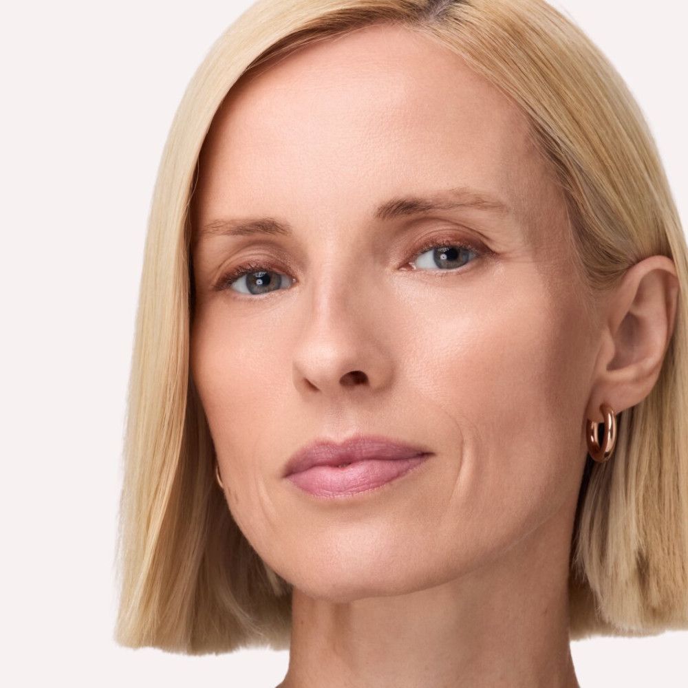 Porträt einer Frau mit blonden Haaren und rosafarbenen Lippen. Sie trägt goldene Creolen.