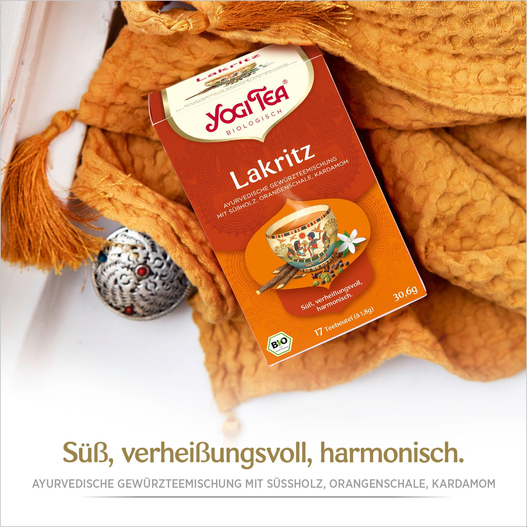 Yogi Tea Lakritz Bio Gewürztee-Packung. Aufdruck: Lakritz, 17 Beutel, 30.6g, Bio-Siegel. Auf orangefarbenem Schal mit Quasten und silbernem Schmuck.
