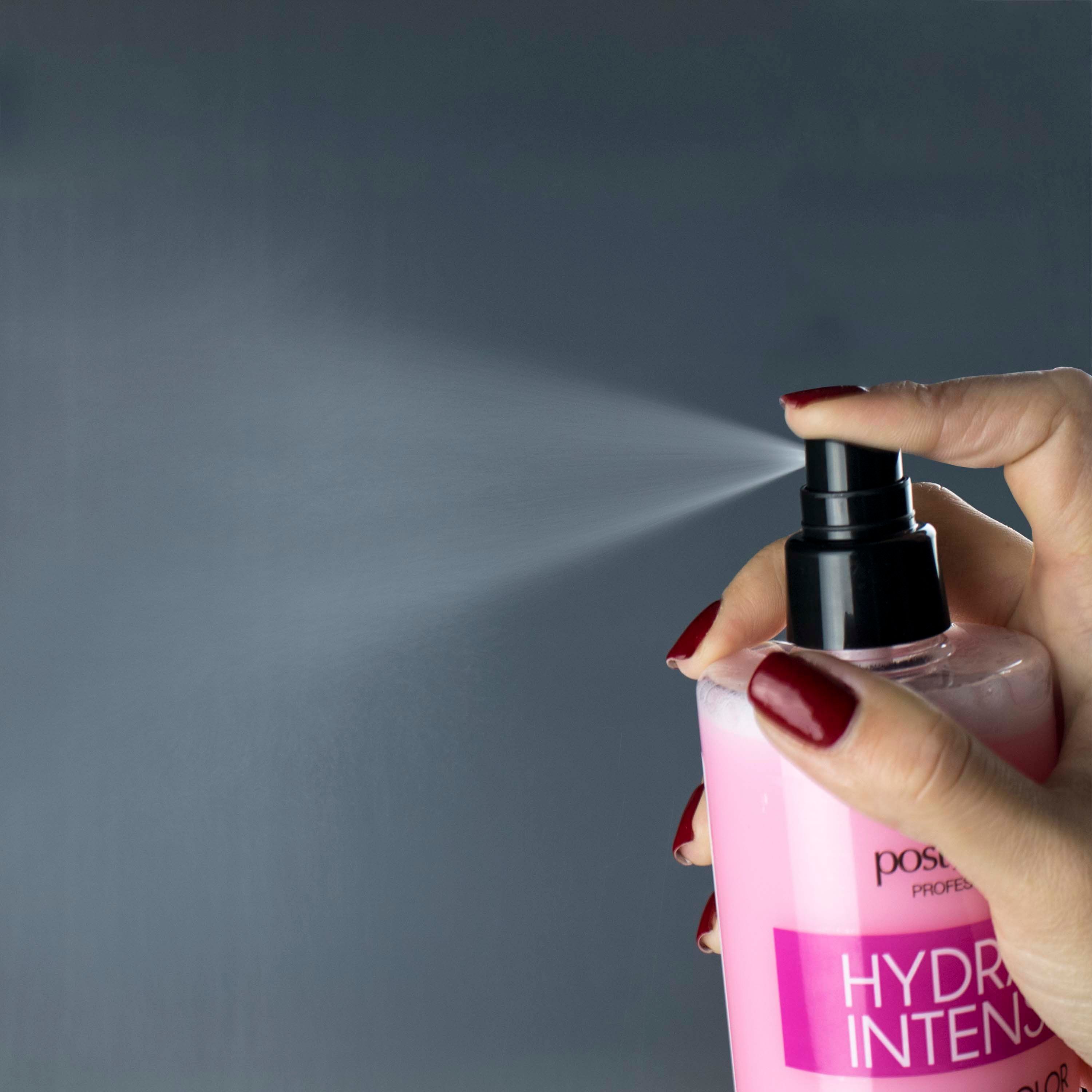 Hand sprüht Flüssigkeit aus einer rosa Flasche. Schwarzer Sprühkopf. Roter Nagellack.