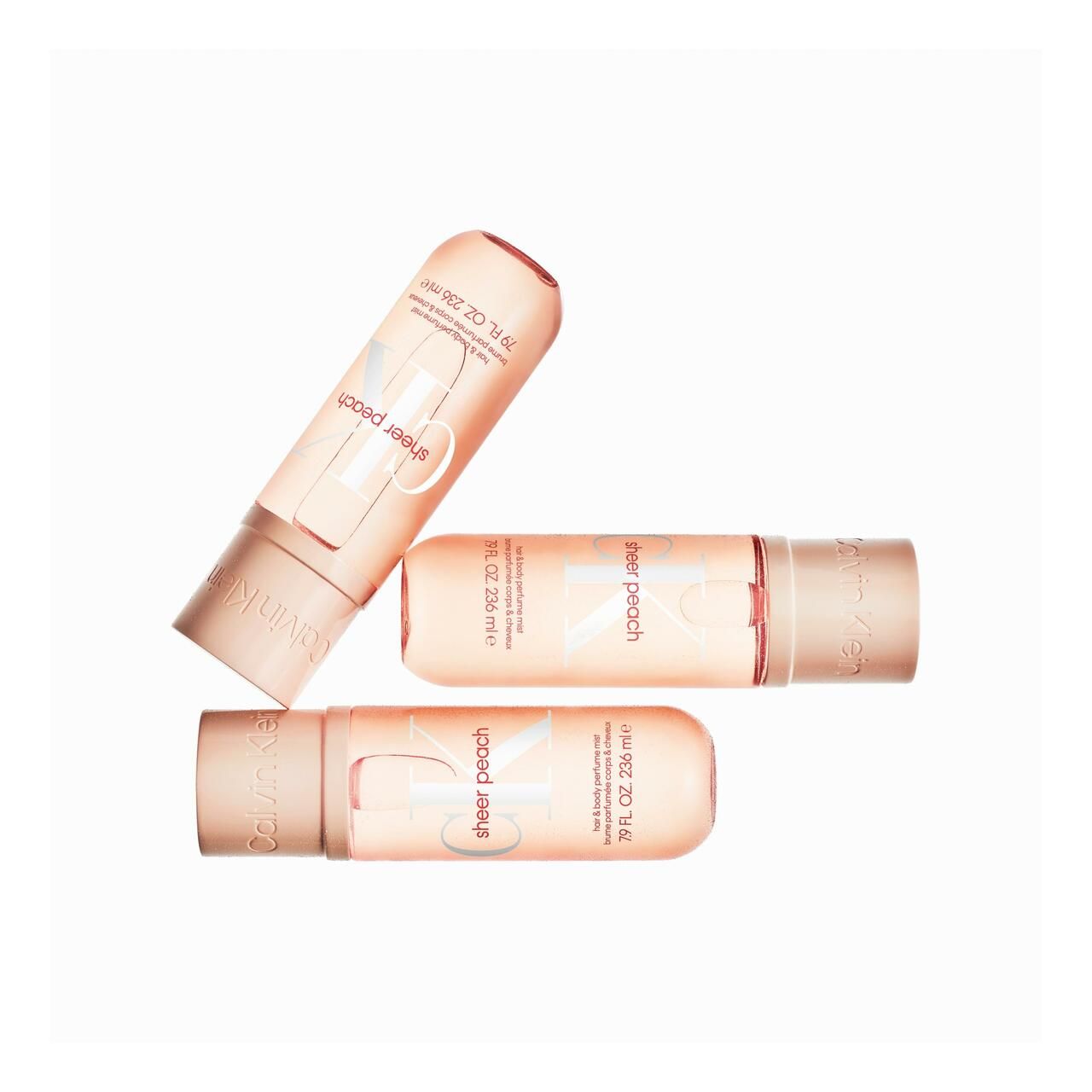 Drei Haar- und Körperspray-Flakons. Aufschrift: sheer peach, Calvin Klein. 79 FL. OZ. 236 ml. Flakons liegen schräg.