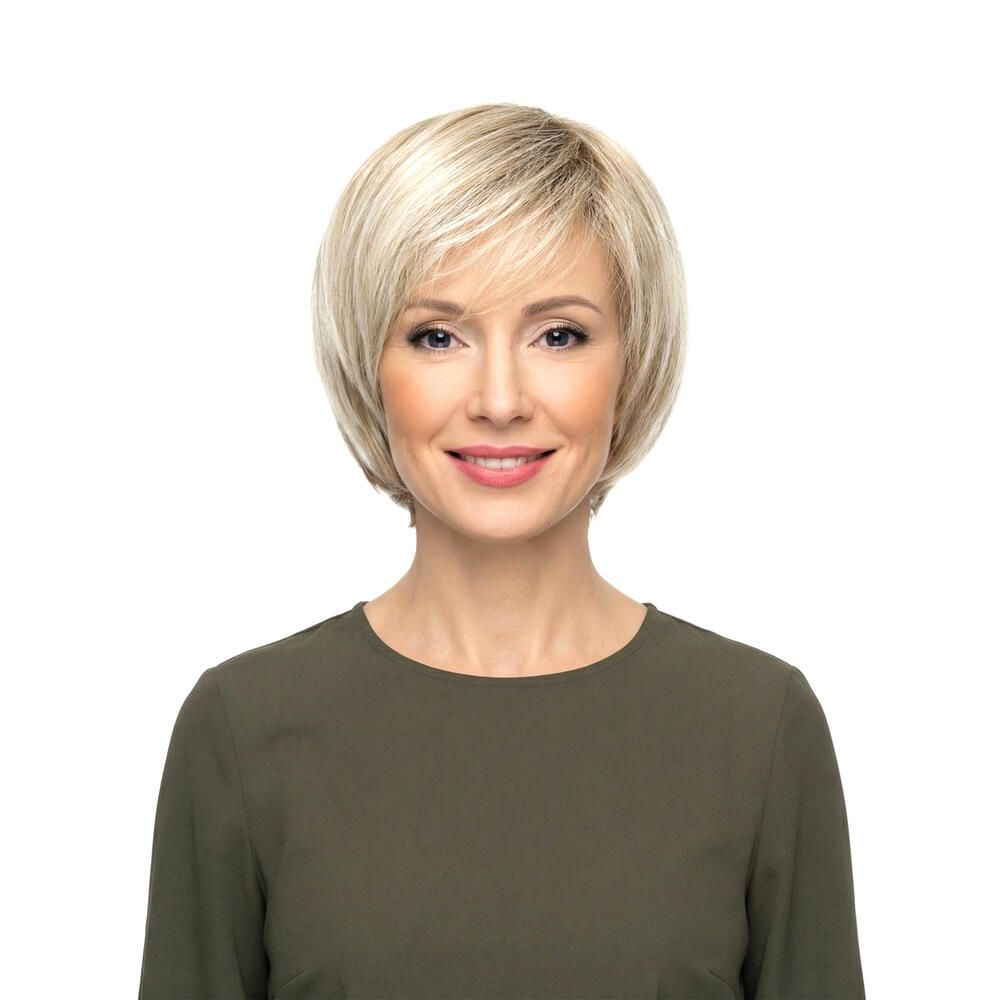 Blond gefärbte Perücke mit kurzem, gewelltem Schnitt. Die Frau trägt ein grünes Oberteil. Frontansicht.