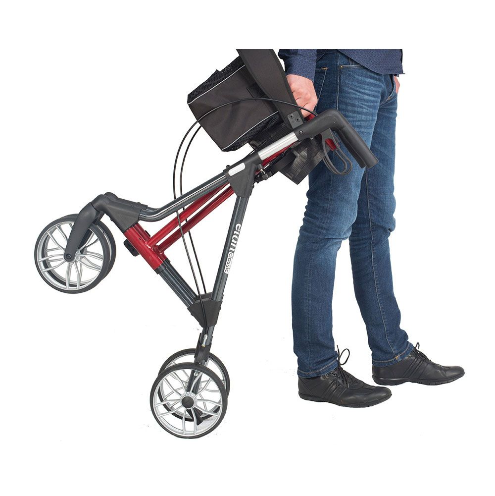 Person trägt einen zusammengeklappten Rollator. Schwarze und rote Elemente. Räder und Handgriffe sichtbar.