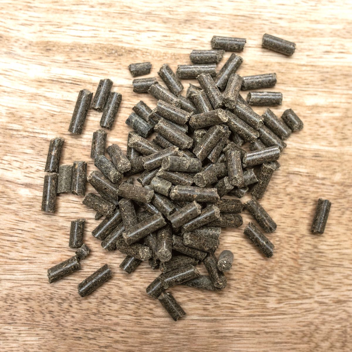 Haufen brauner Pellets auf Holzuntergrund. Zylindrische Form, unterschiedliche Größen.