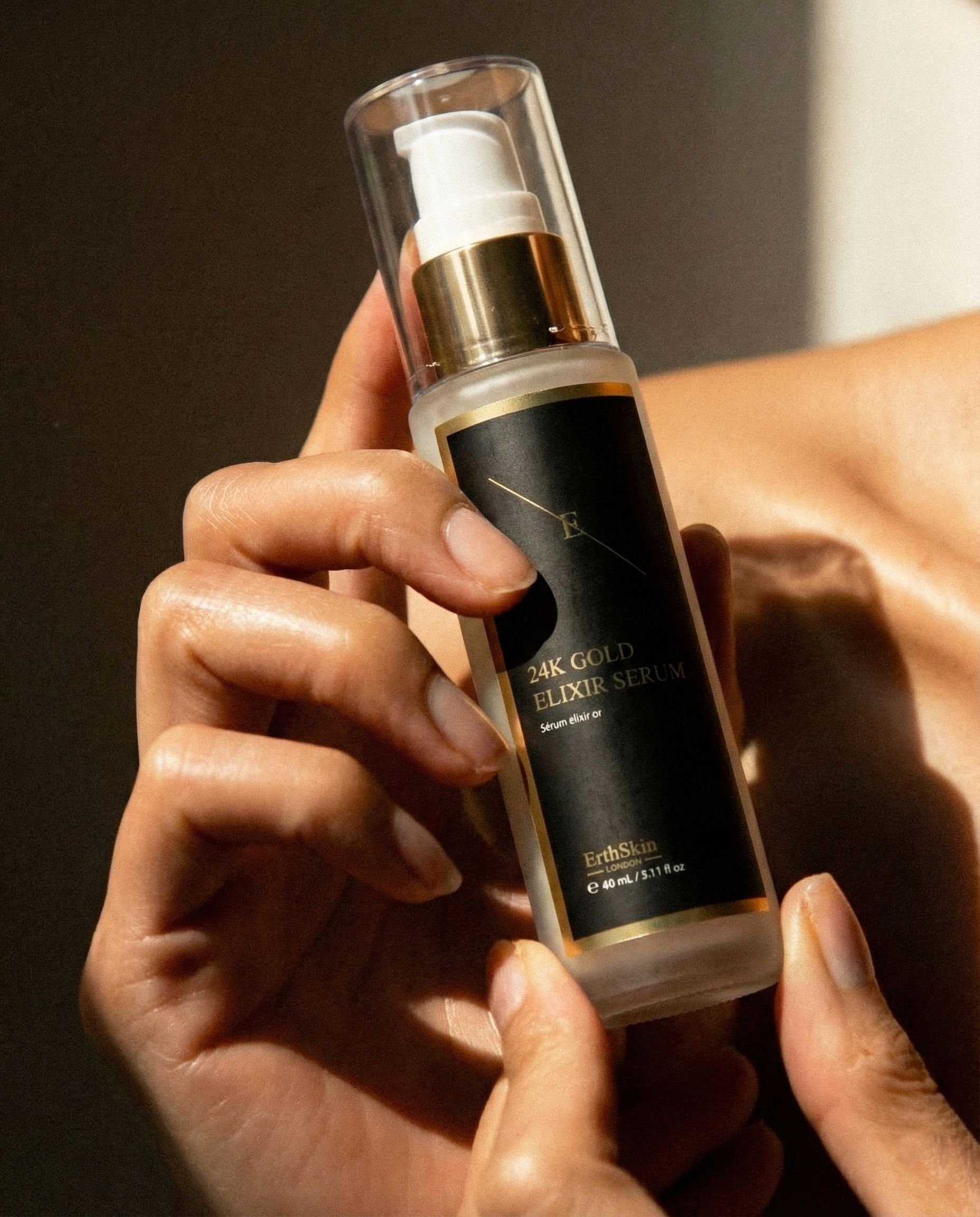 Hände halten eine Flasche 24K Gold Elixir Serum.