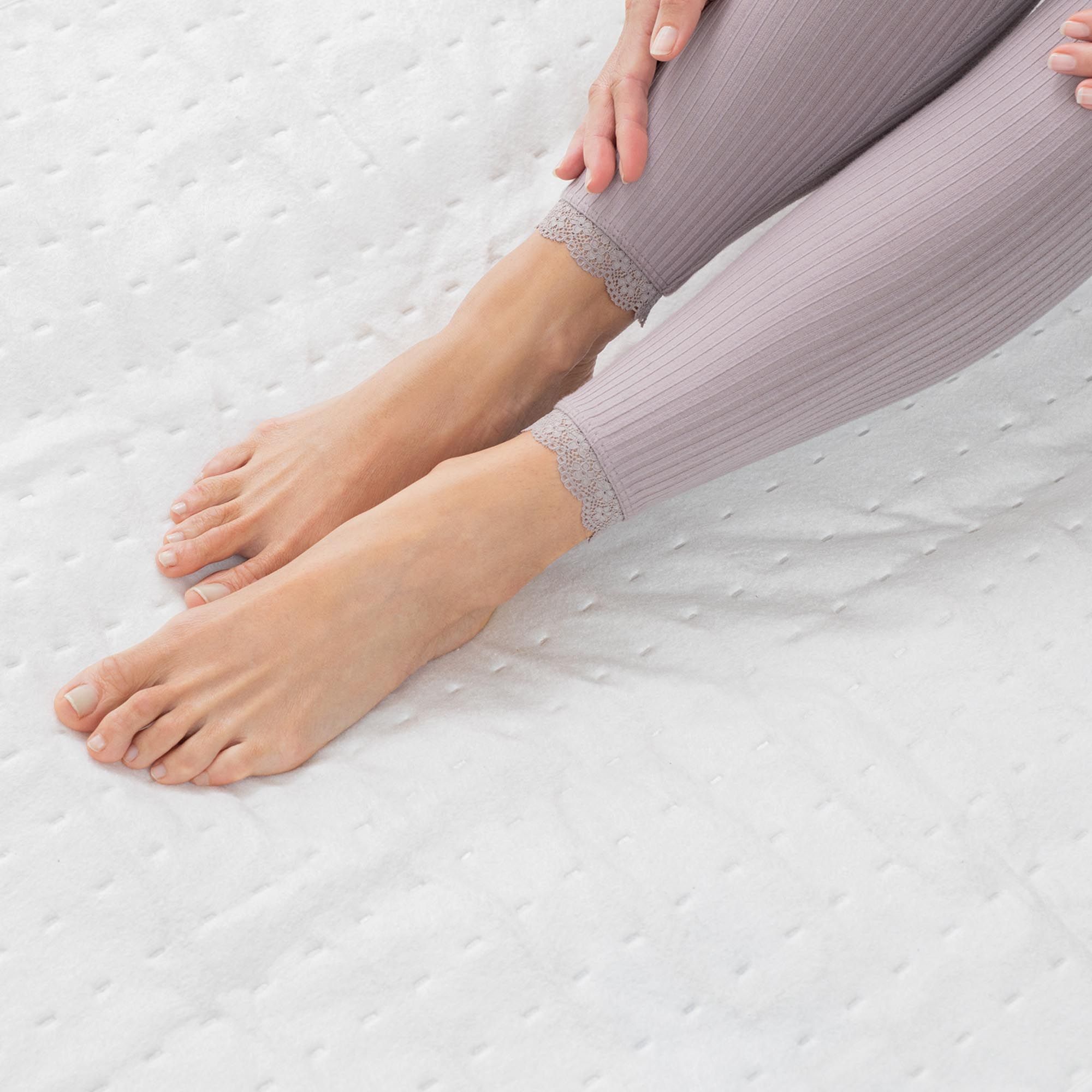 Gros plan : pieds sur une couverture chauffante blanche. La personne porte un legging.