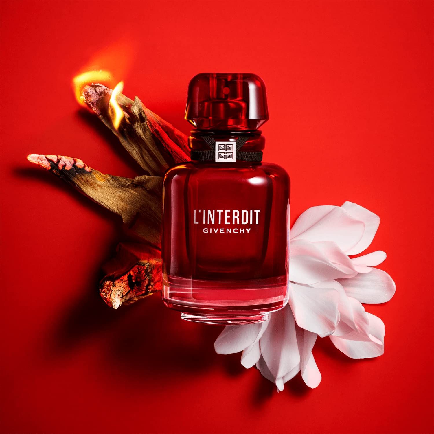Rote Flasche mit schwarzem Band und silbernem Verschluss, umgeben von einer weißen Blume und Holz auf rotem Hintergrund.