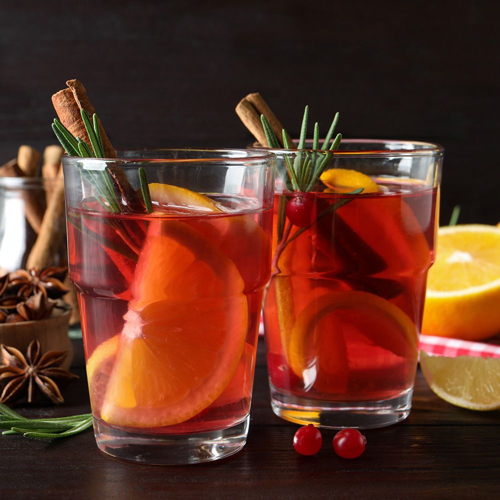 Zwei Gläser Glühwein mit Orangen, Zimtstangen und Rosmarin. Dunkler Hintergrund.