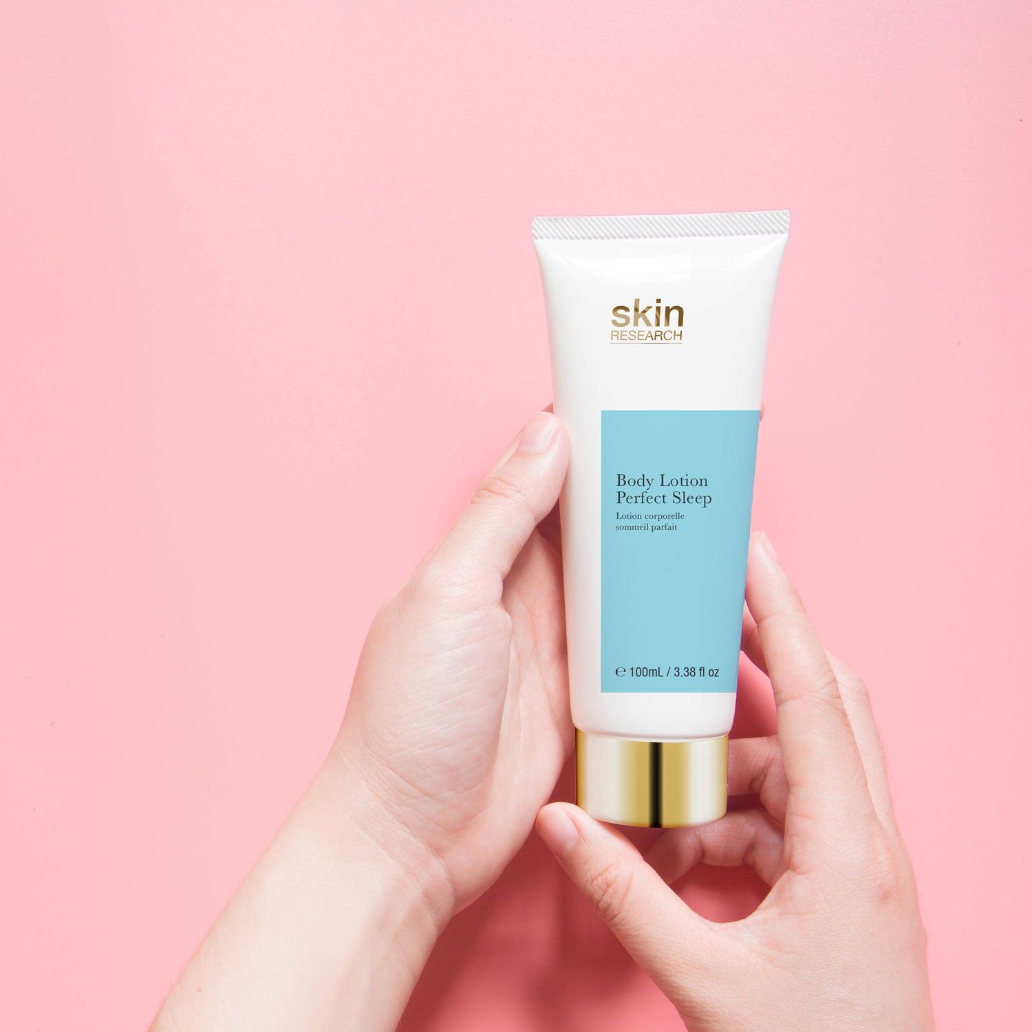 Hände halten Creme-Tube. Aufschrift: Skin Research, Body Lotion Perfect Sleep. Hintergrund: rosa.