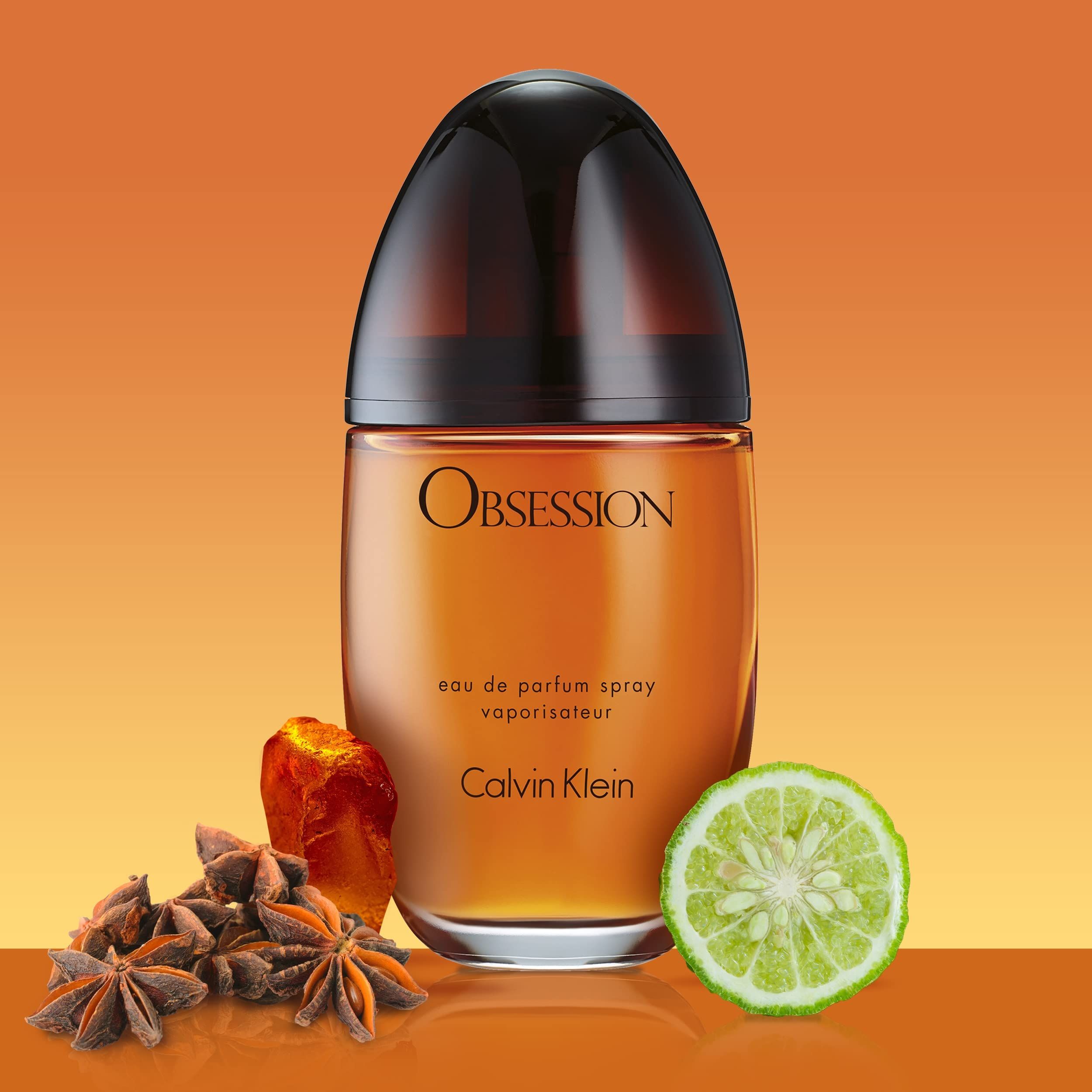 Parfümflasche mit Obsession-Schriftzug, umgeben von Sternanis und Zitronenstückchen auf orangefarbenem Hintergrund.