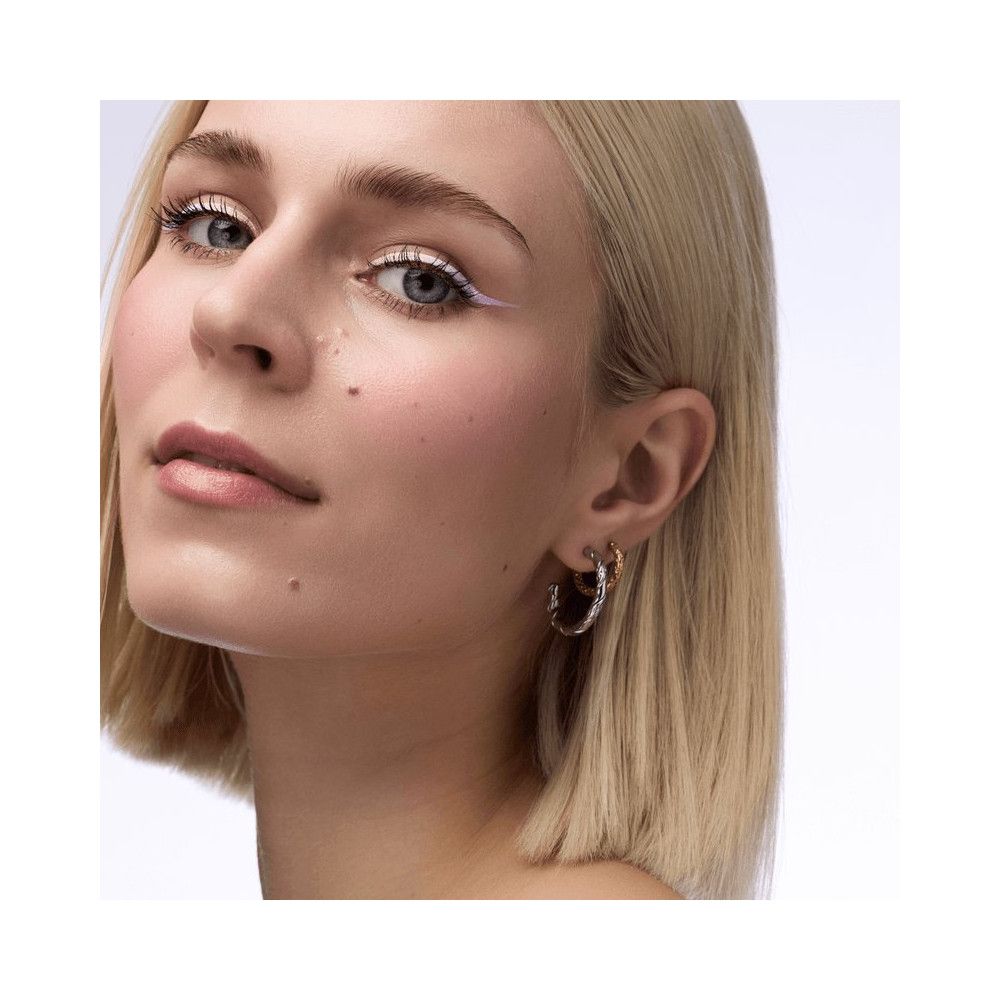 Nahaufnahme einer Frau mit weißem Eyeliner. Sie trägt Ohrringe.