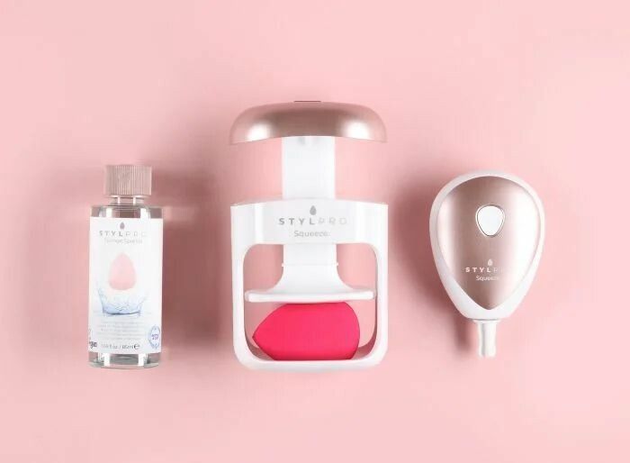 Reinigungsgerät, Reinigungsflüssigkeit und separates Gerät. Gerät: weiß, roségold. Flüssigkeit: Flasche mit Etikett. Hintergrund: rosa.