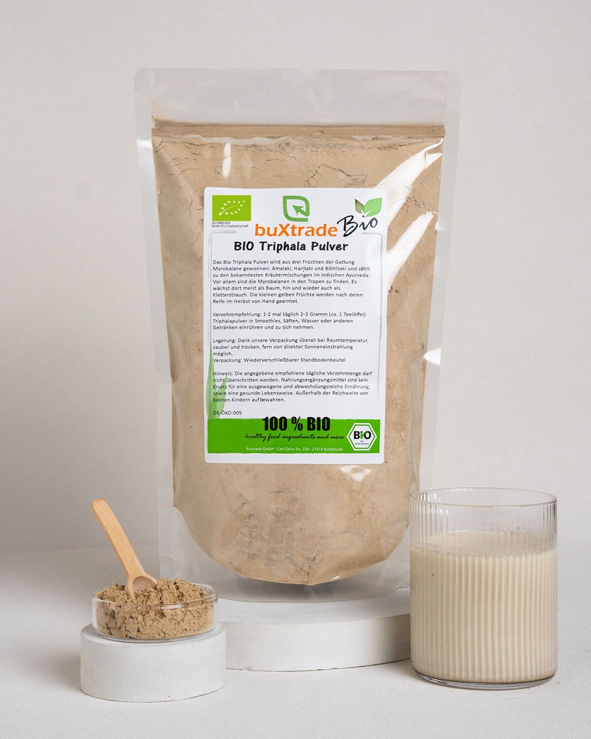 Bio Triphala Pulver in einem Beutel, daneben eine Schale mit Pulver und ein Glas mit Getränk.
