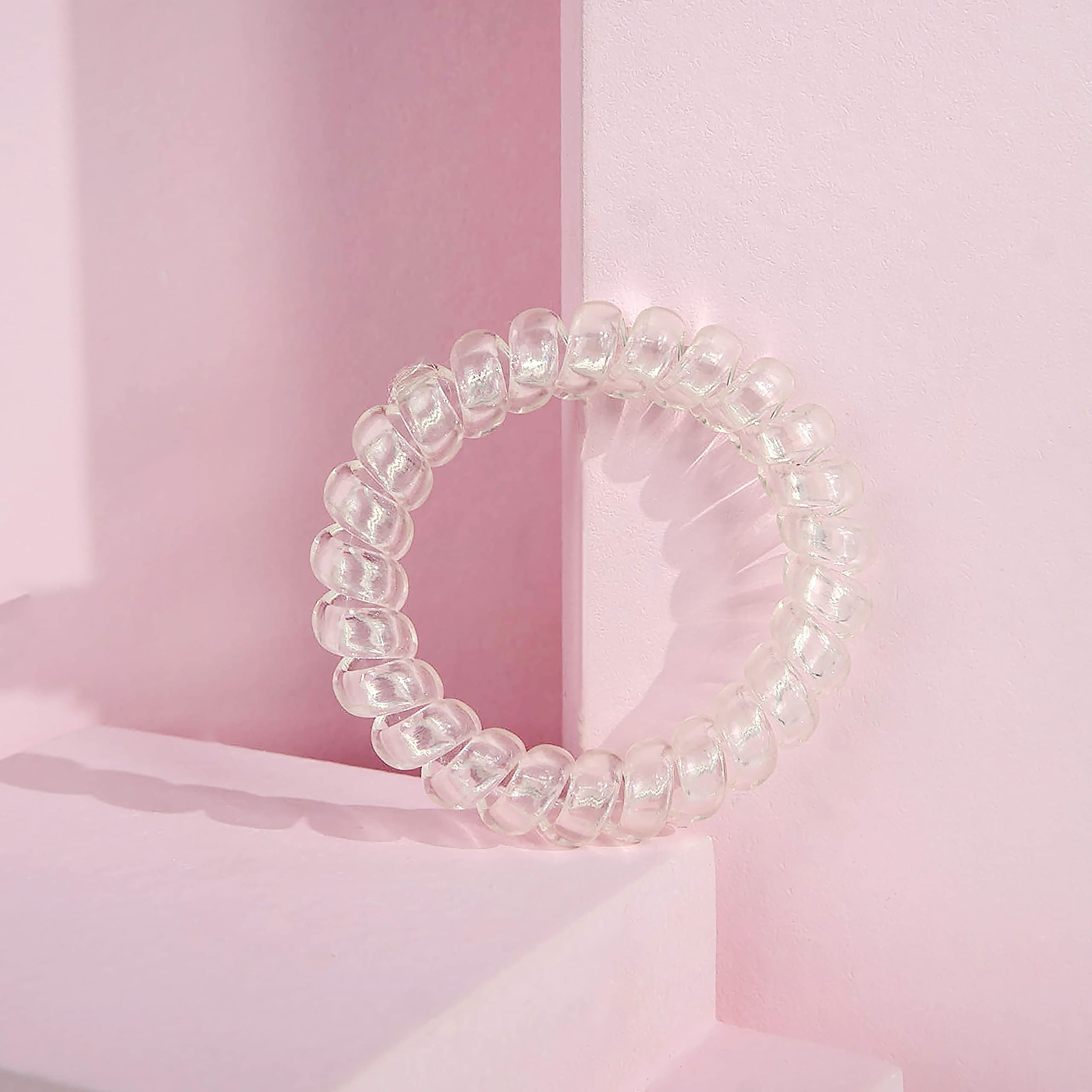 Haargummi in Spiralform, transparent. Auf rosa Oberfläche platziert.