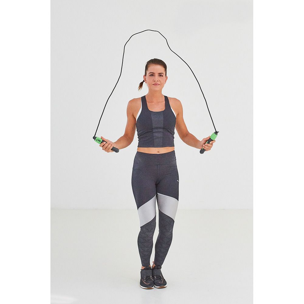 Frau springt mit einem schwarzen Springseil. Griffe grün. Person trägt Sportkleidung.