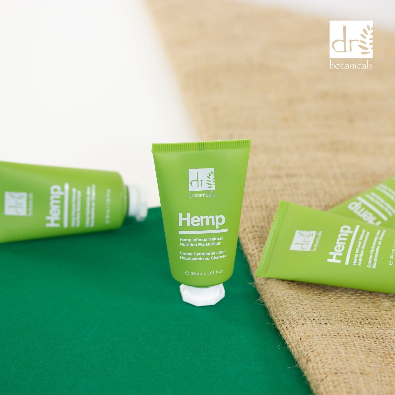 Mehrere grüne Tuben mit weißem Deckel. Aufschrift: Hemp, Hemp Infused Natural Nutrition Moisturiser, 30 ml. Auf Jutegewebe und grünem Untergrund.