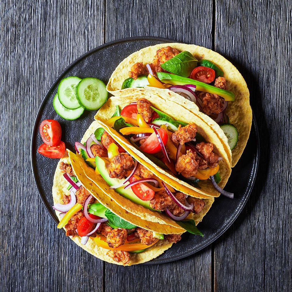 Drei Tacos auf einem Teller. Gefüllt mit Gemüse und Fleisch. Draufsicht.