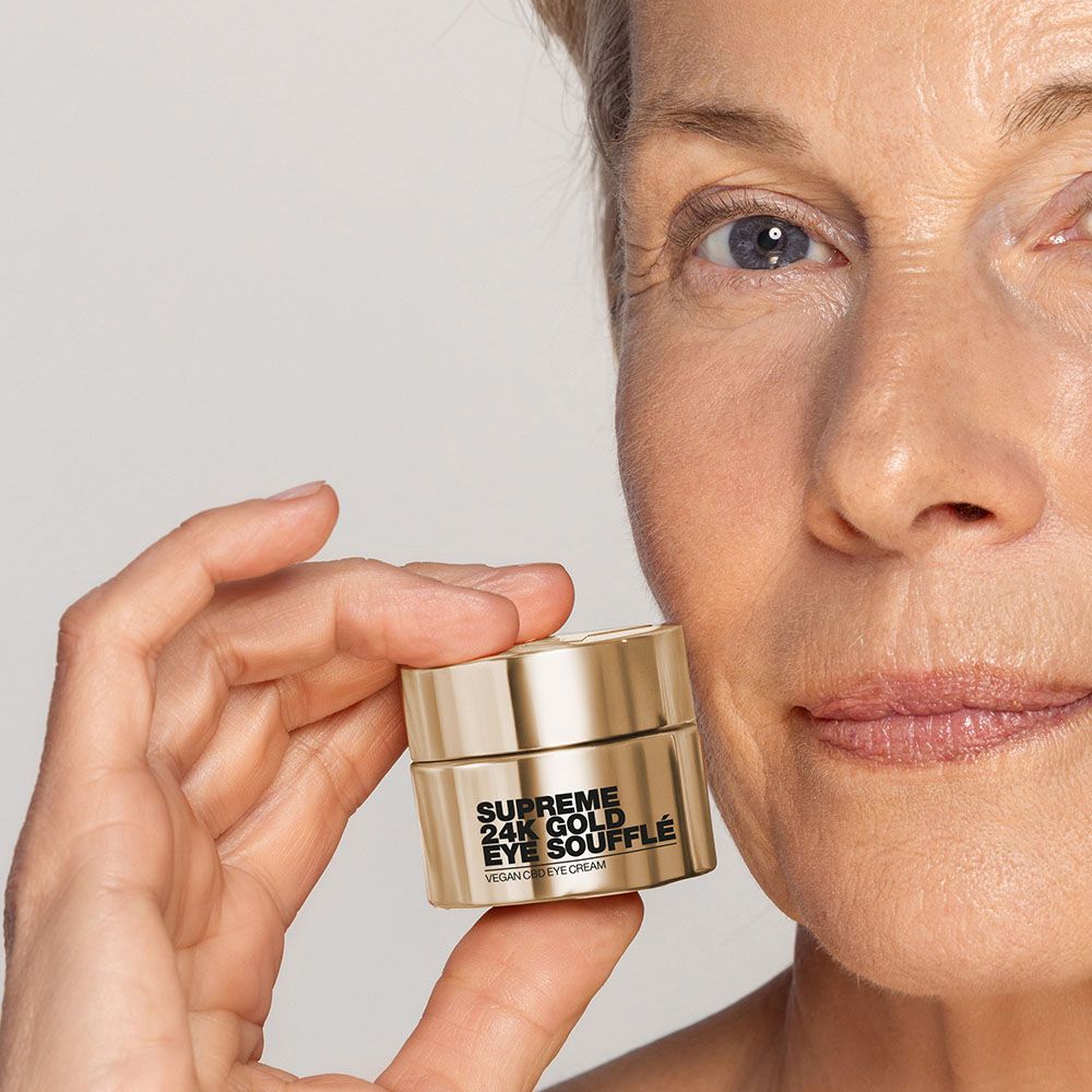 Frau hält goldfarbenen Tiegel. Aufschrift: Supreme 24K Gold Eye Soufflé, Vegan Eye Cream.