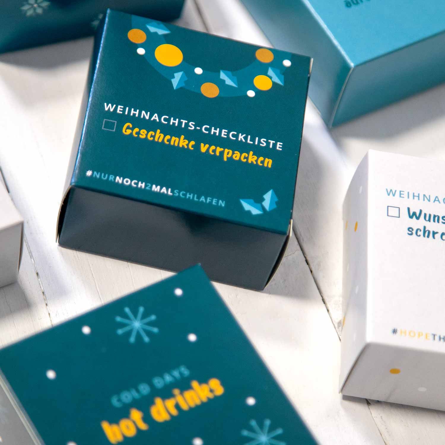Kleine, quadratische Schachteln mit Aufdruck. Text: WEIHNACHTS-CHECKLISTE, Geschenke verpacken, #nurnochmalschlafen, COLD DAYS HOT DRINKS.