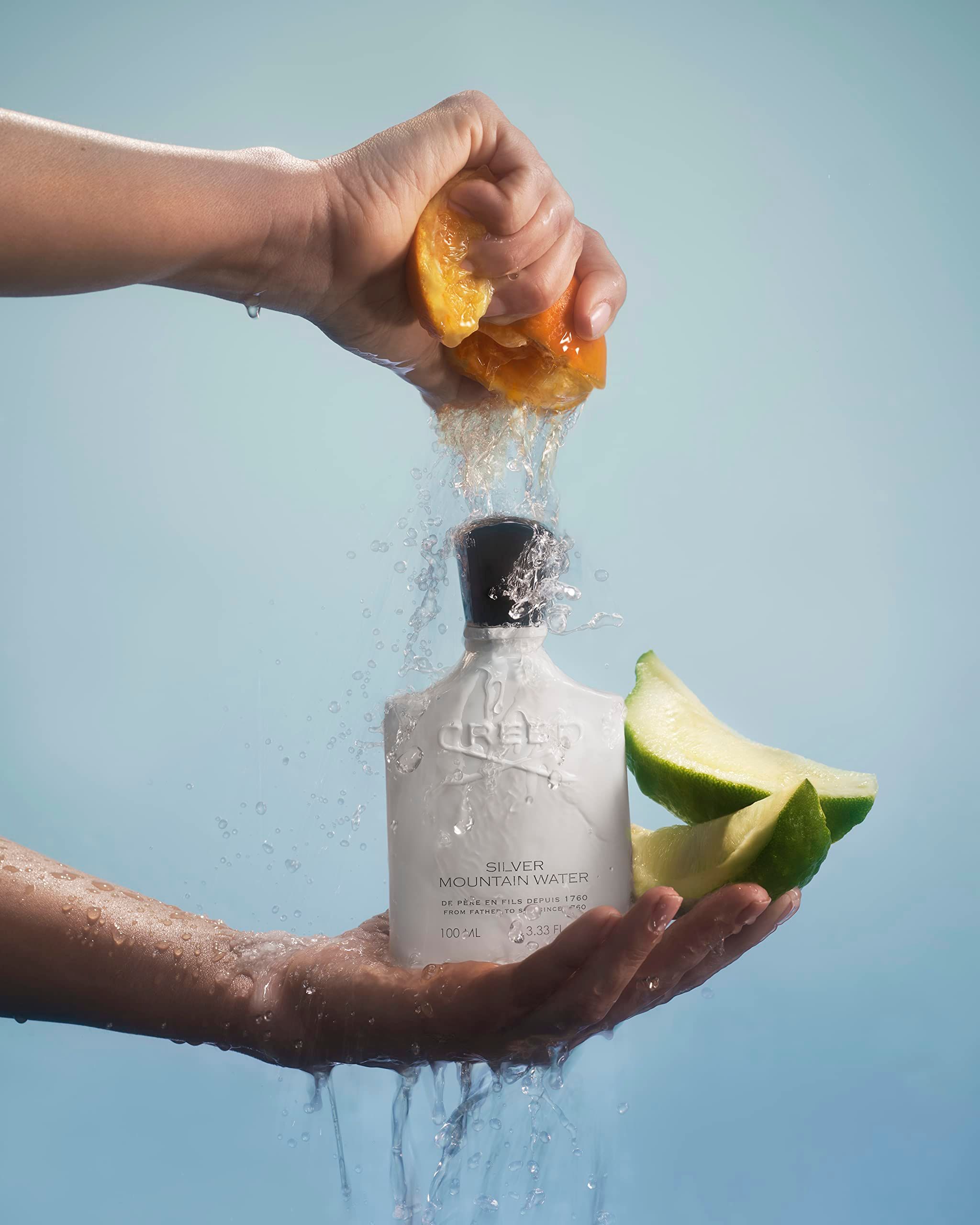 Hände drücken eine Orange über einer Parfumflasche. Aufschrift: Creed Silver Mountain Water.