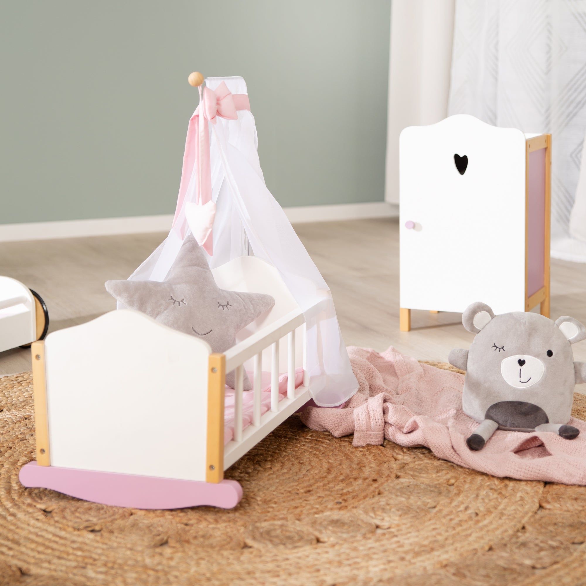 Puppenwiege mit Zubehör: Schrank, Teddybär und Kissen. Auf einem runden Teppich.