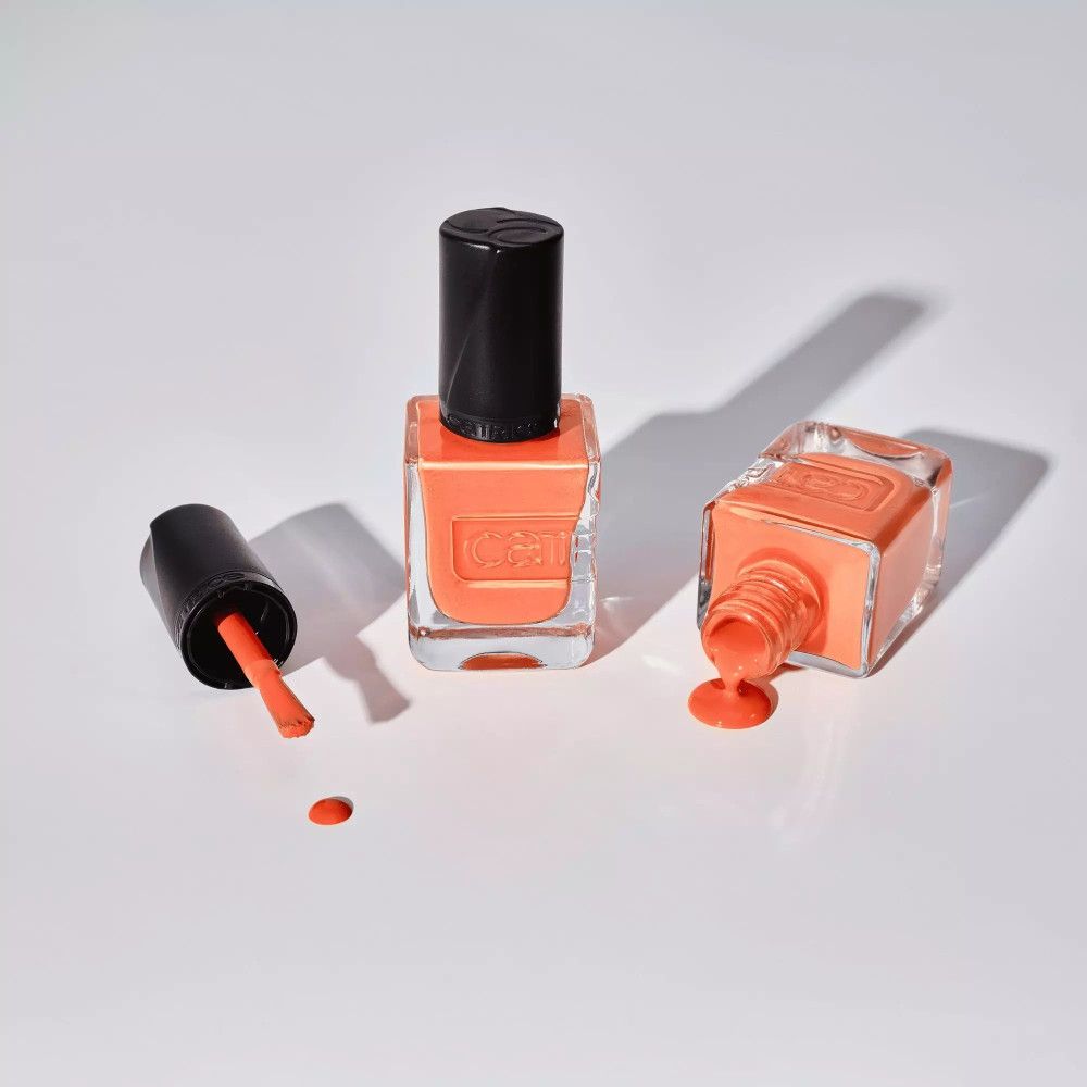 Nagellackflaschen mit orangefarbenem Inhalt. Eine Flasche auf dem Kopf, eine mit Pinsel. Schwarze Deckel.